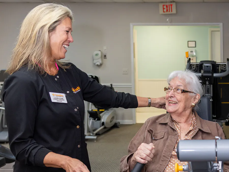 A woman smiling with a therapist while completing leg exercises.